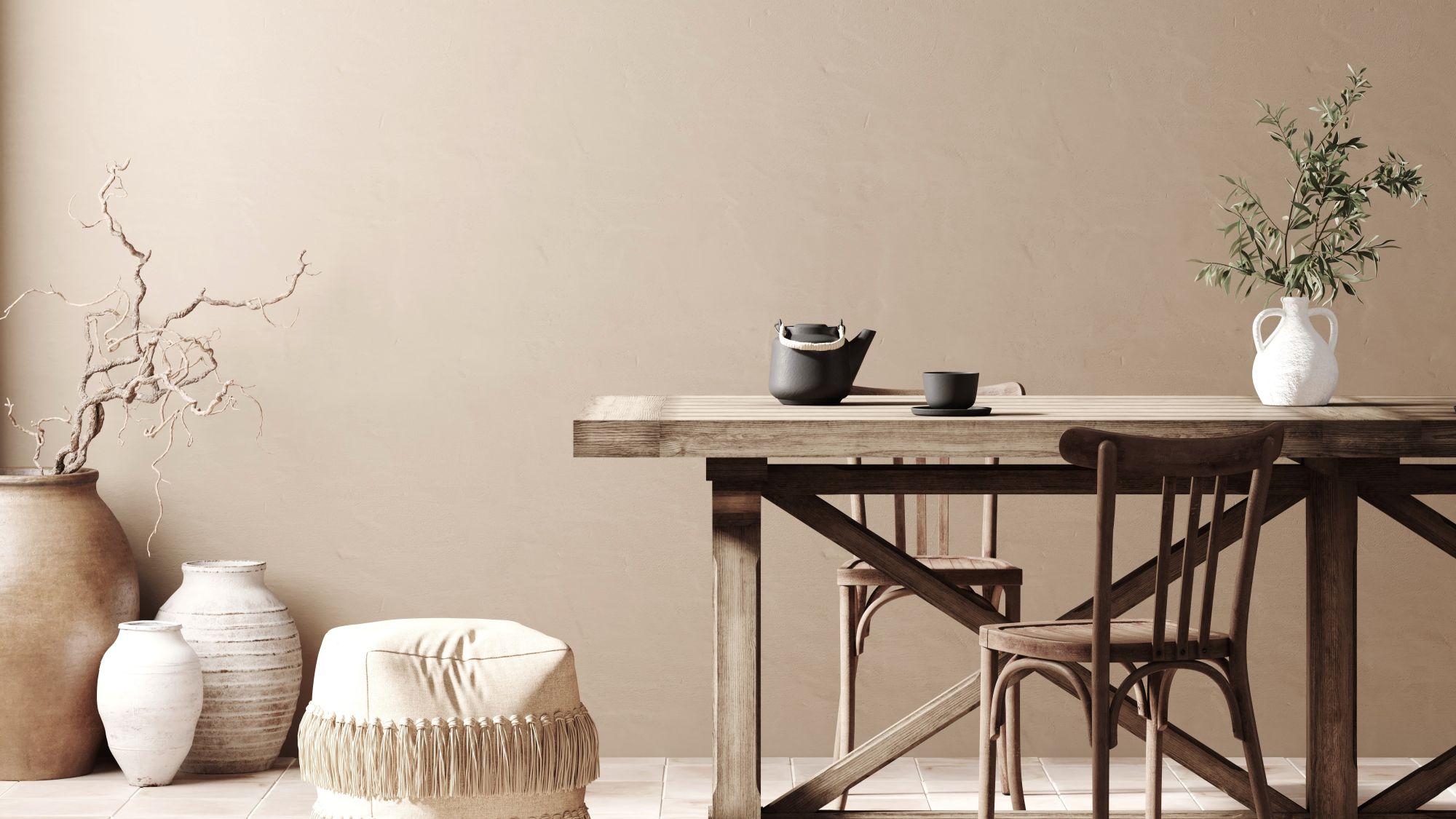 A dining room featuring a long, natural wood dining table and chairs. The walls are a warm, light taupe colour. On the left, a collection of large, textured vases hold decorative branches.