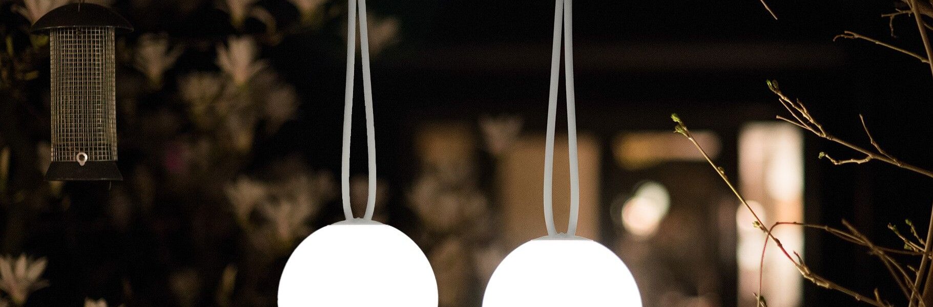 An illuminated spherical outdoor light hung from a tree branch