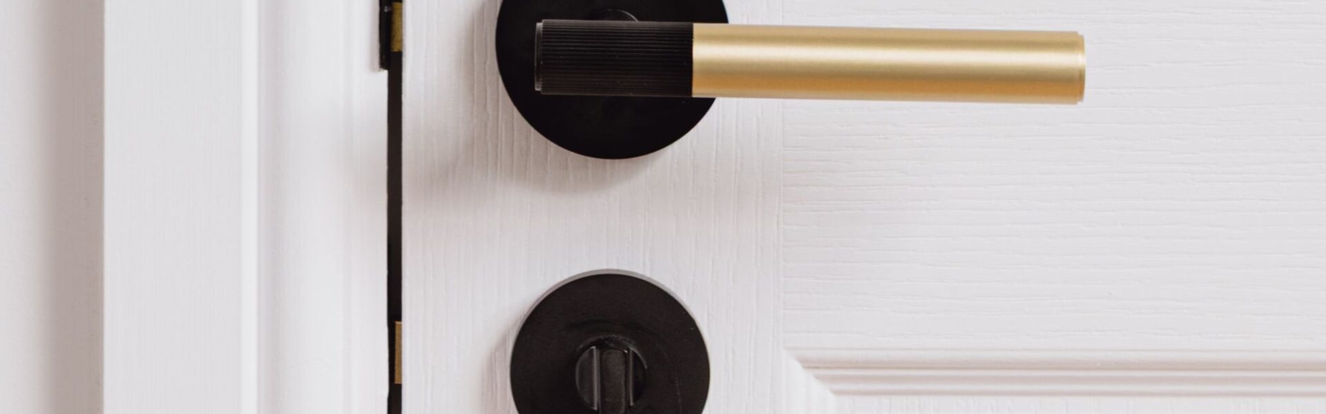 A linear lever handle with a modern, two-tone finish. It features a gold cylindrical main grip and a black or matte black accent on the end of the grip, which appears to have a subtle ribbed or textured surface. The handle is mounted on a round black rose
