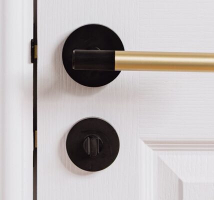 A linear lever handle with a modern, two-tone finish. It features a gold cylindrical main grip and a black or matte black accent on the end of the grip, which appears to have a subtle ribbed or textured surface. The handle is mounted on a round black rose