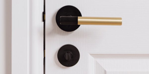 A linear lever handle with a modern, two-tone finish. It features a gold cylindrical main grip and a black or matte black accent on the end of the grip, which appears to have a subtle ribbed or textured surface. The handle is mounted on a round black rose