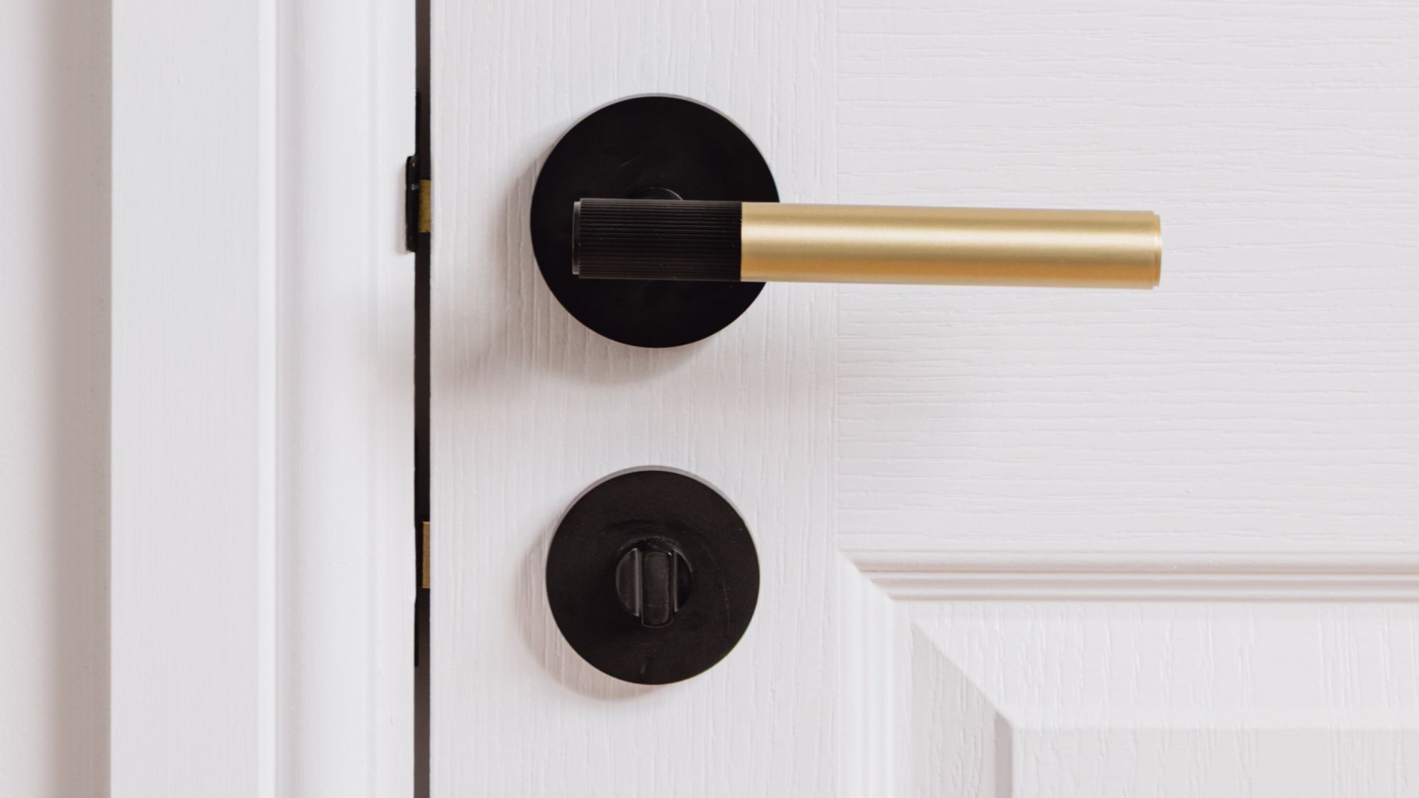 A linear lever handle with a modern, two-tone finish. It features a gold cylindrical main grip and a black or matte black accent on the end of the grip, which appears to have a subtle ribbed or textured surface. The handle is mounted on a round black rose
