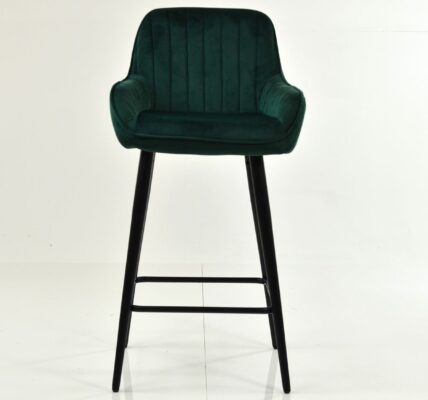A single, modern bar stool with a deep green, vertically channel-tufted velvet seat and backrest, resting on tall, slim black wooden legs.