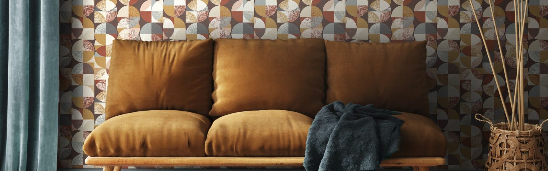 A living room with a three-seater sofa, wooden parquet flooring and denim blue curtains. The background features a geometric wallpaper in different shades of brown, orange and amber