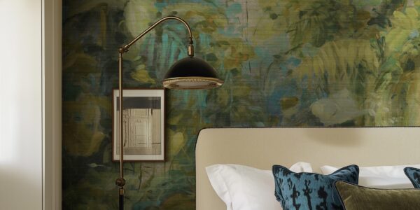A bedroom with a textured green and gold abstract botanical wallpaper mural, featuring a bed with a beige headboard and a black-and-brass floor lamp.