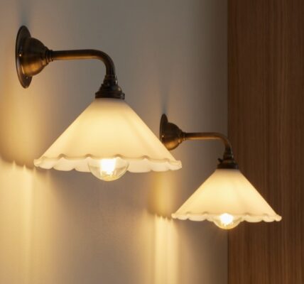 A wall light which features a frilled, scalloped edge, a cone Shape and an antique finish. The arm and wall plate have a warm, aged metal look.