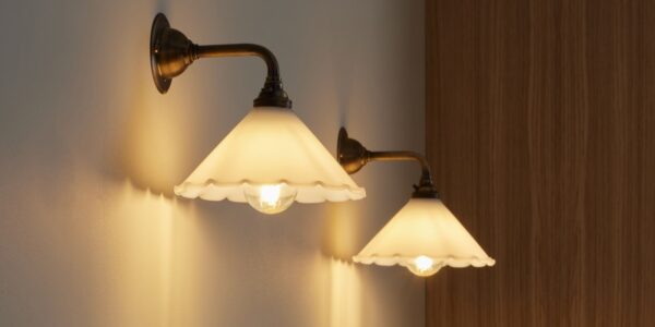 A wall light which features a frilled, scalloped edge, a cone Shape and an antique finish. The arm and wall plate have a warm, aged metal look.