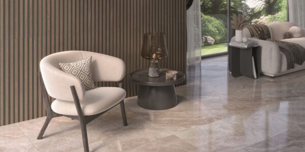 A luxurious, modern living space featuring a creamy white upholstered armchair, a ribbed wood accent wall, and glossy light-brown marble-look floor tiles. A dark round side table with a decorative lamp sits next to the chair, and a large window looks out onto a green garden.