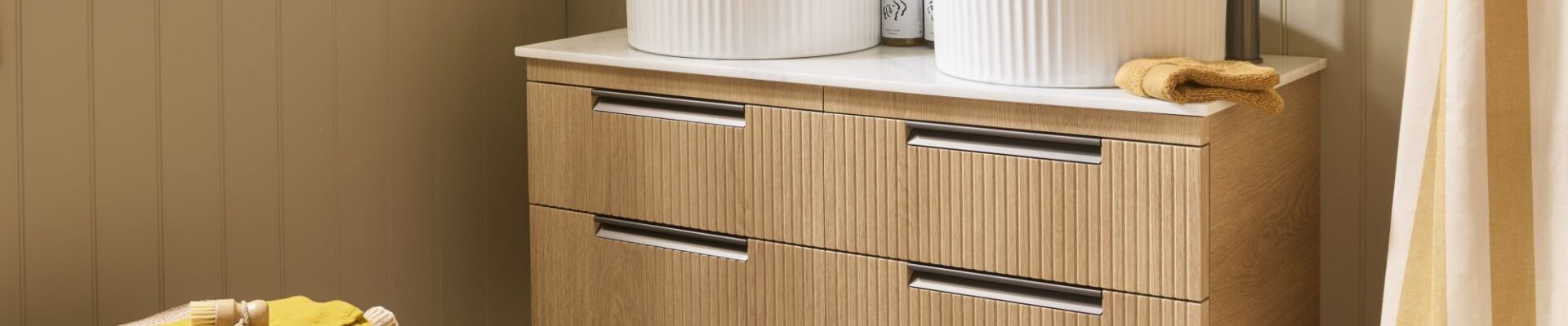 The image shows a wall-mounted vanity unit in a Swiss Oak finish with a fluted (reeded) texture on the drawer fronts. It features a double sink design with two white, ribbed/fluted countertop basins and two tall, modern gunmetal taps.