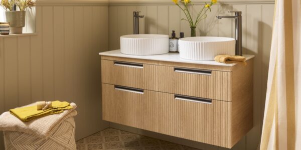 The image shows a wall-mounted vanity unit in a Swiss Oak finish with a fluted (reeded) texture on the drawer fronts. It features a double sink design with two white, ribbed/fluted countertop basins and two tall, modern gunmetal taps.