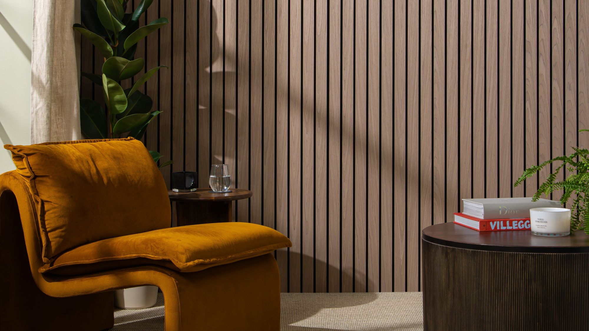 The background is dominated by a wall covered in vertical, dark walnut-coloured wooden slats set against a dark backing, creating a strong sense of texture and modern design. In the foreground on the left is a large, inviting armchair upholstered in a rich, burnt orange/mustard velvet. Its rounded, contemporary shape adds a soft contrast to the straight lines of the wall.
