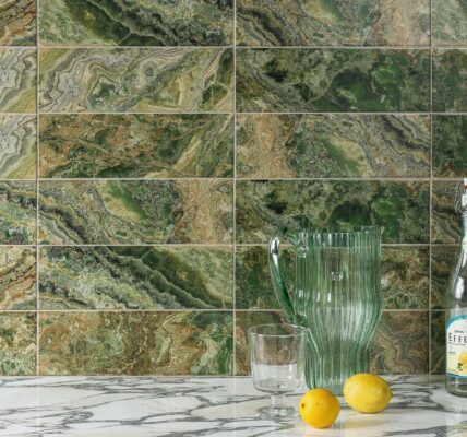 A wall tiled with rectangular, high-gloss tiles that have a dramatic, variegated pattern resembling green and brown natural stone. The dominant colours are various shades of rich green, from deep forest green to lighter lime green, mixed with earthy browns and occasional white veining, creating a strata or layered look.