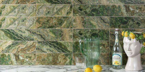 A wall tiled with rectangular, high-gloss tiles that have a dramatic, variegated pattern resembling green and brown natural stone. The dominant colours are various shades of rich green, from deep forest green to lighter lime green, mixed with earthy browns and occasional white veining, creating a strata or layered look.