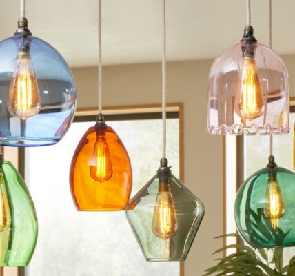 The image shows a cluster of seven colourful glass pendant lights hanging from the ceiling, likely over a kitchen island or dining area. Each pendant has a distinct shape and colour, creating a vibrant, eclectic look.