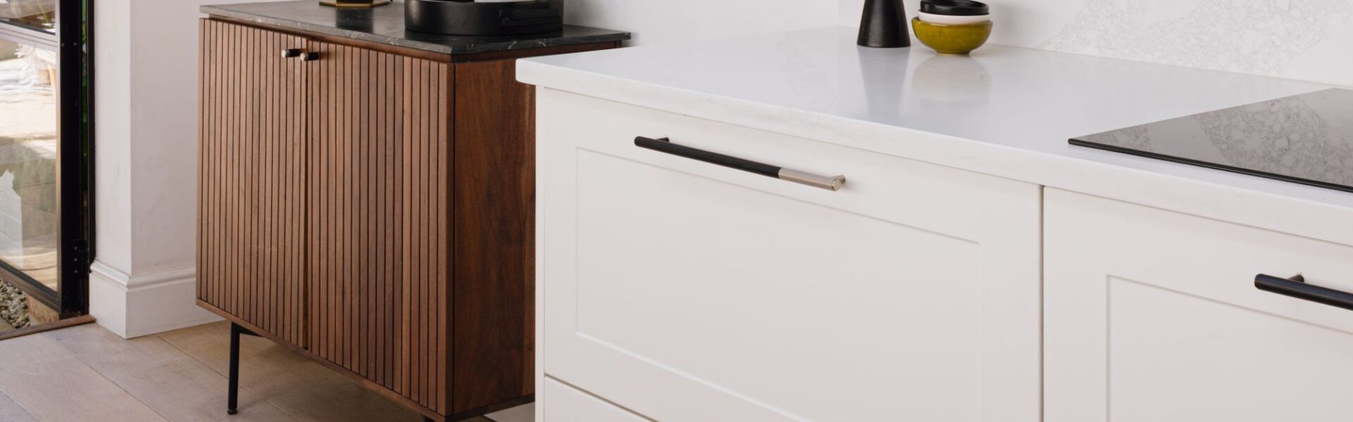 This image shows white kitchen cabinets with recessed panels. The cabinets are fitted with long, linear cabinet handles that have a two-tone finish - black with a silver tip. A white countertop sits above the cabinets.