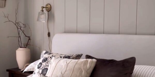 The wall features vertical V-groove panelling painted a light, neutral grey/taupe colour. The panelling extends upwards, perhaps to meet a picture rail or just below the ceiling, creating a backdrop for the bed.