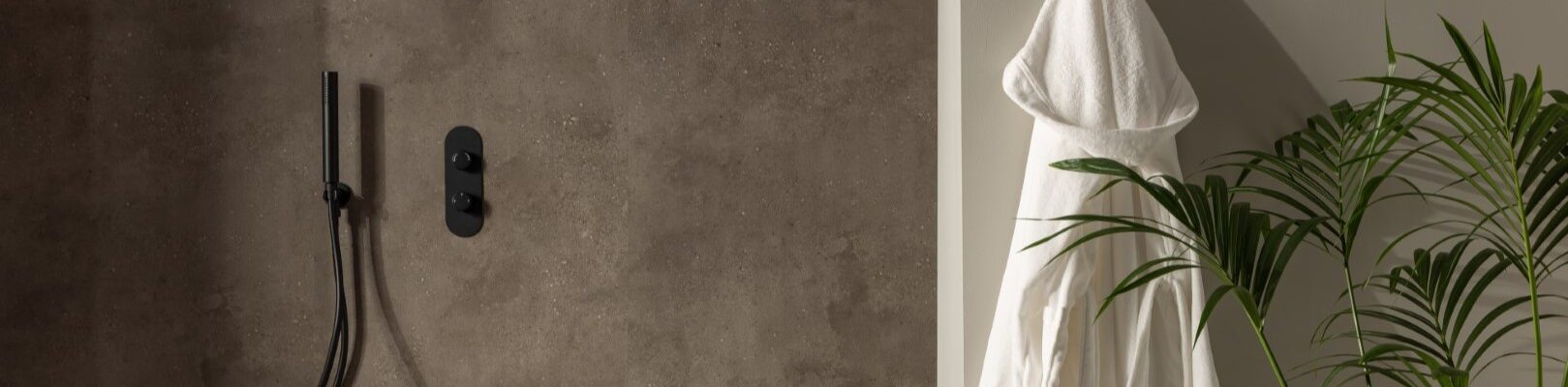 A shower wall clad in a dark, mottled, stone-effect panel. It has a warm, earthy brown/grey tone with slight texture variations. The shower fixtures—including the rainfall shower head, the handheld shower wand, and the control panel—are all in a matte black finish, providing a stark, contemporary contrast against the stone panel.