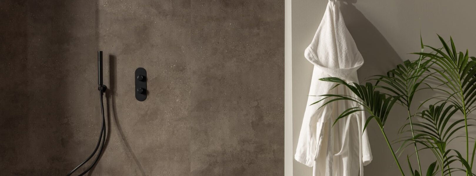 A shower wall clad in a dark, mottled, stone-effect panel. It has a warm, earthy brown/grey tone with slight texture variations. The shower fixtures—including the rainfall shower head, the handheld shower wand, and the control panel—are all in a matte black finish, providing a stark, contemporary contrast against the stone panel.