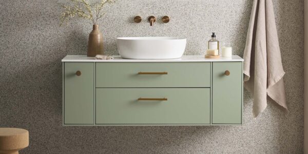 A wall-mounted vanity in a soft, muted sage green or light olive colour. It has two central drawers with long, horizontal brass or gold-tone handles.