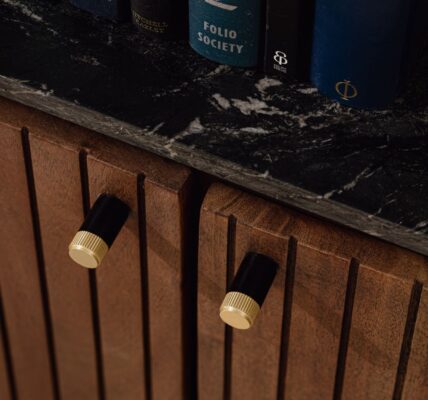 Close-up of a fluted wooden cabinet with two dual-tone cylindrical pulls in matte black and knurled gold, topped with a black marble counter.