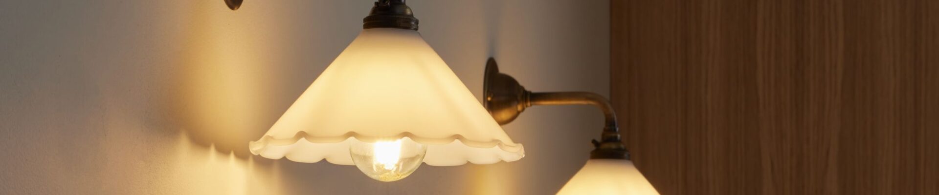 Two contemporary brass wall lights with opal frilled glass shades mounted on a white wall.