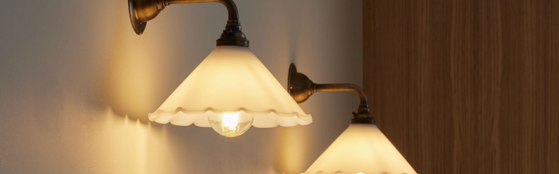 Two contemporary brass wall lights with opal frilled glass shades mounted on a white wall.