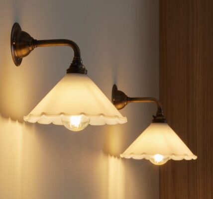 Two contemporary brass wall lights with opal frilled glass shades mounted on a white wall.