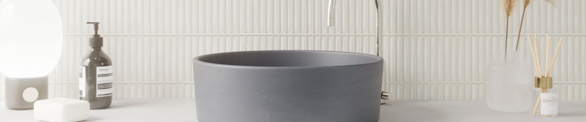 A modern bathroom vanity featuring a matte charcoal vessel sink on a concrete countertop against a white vertical Kit Kat finger tile backsplash.