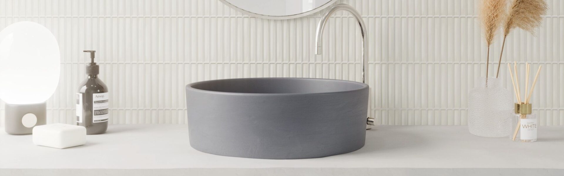A modern bathroom vanity featuring a matte charcoal vessel sink on a concrete countertop against a white vertical Kit Kat finger tile backsplash.