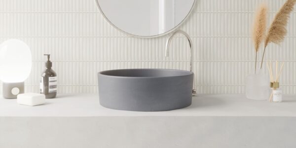 A modern bathroom vanity featuring a matte charcoal vessel sink on a concrete countertop against a white vertical Kit Kat finger tile backsplash.