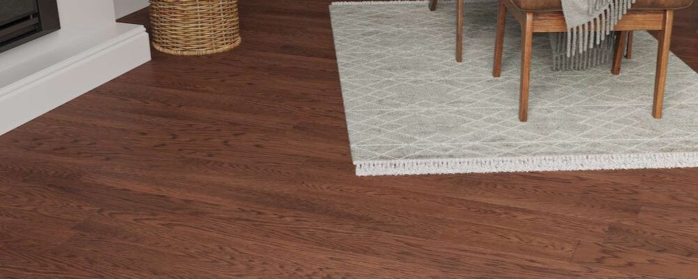 A cosy living room setting featuring Lusso Modena Luxe Oakmere engineered oak flooring in a rich, dark walnut finish. The dark wood planks are paired with a white fireplace hearth, a woven log basket, and a light grey patterned rug under mid-century modern furniture.