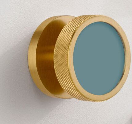 An extreme close-up of a modern, brushed gold brass mortice door knob mounted on a white door. The knob features a distinctive knurled texture around its edge for grip and a flat, circular face inset with a matte teal-blue colour.
