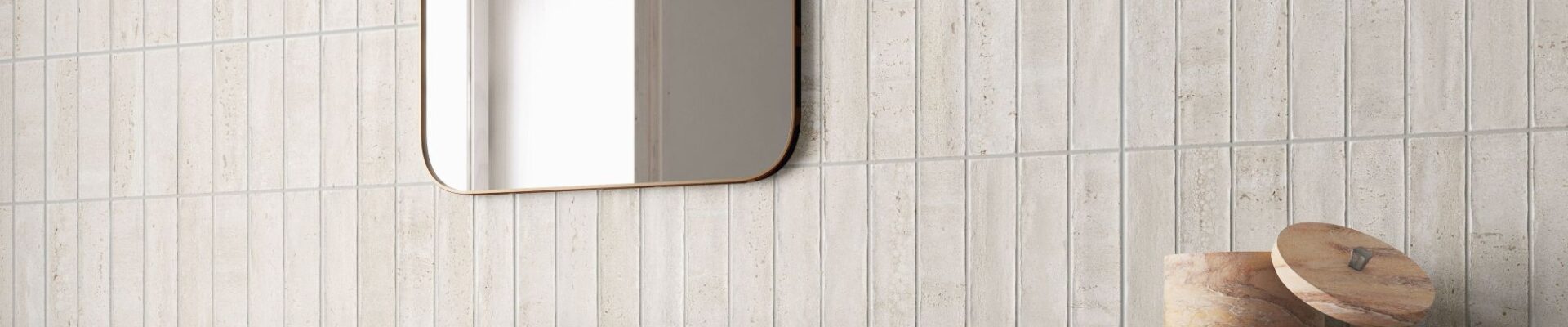 A contemporary bathroom scene featuring light beige, travertine-style wall tiles. The top half of the wall is composed of narrow, vertical kit-kat tiles, while the bottom half consists of large-format horizontal slabs with subtle stone veining.