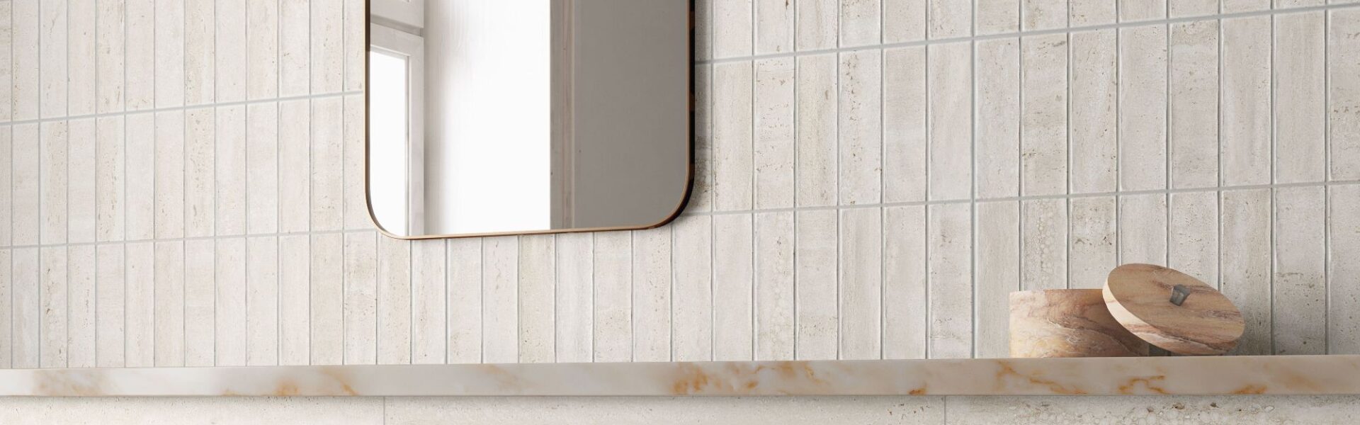 A contemporary bathroom scene featuring light beige, travertine-style wall tiles. The top half of the wall is composed of narrow, vertical kit-kat tiles, while the bottom half consists of large-format horizontal slabs with subtle stone veining.