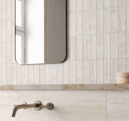 A contemporary bathroom scene featuring light beige, travertine-style wall tiles. The top half of the wall is composed of narrow, vertical kit-kat tiles, while the bottom half consists of large-format horizontal slabs with subtle stone veining.