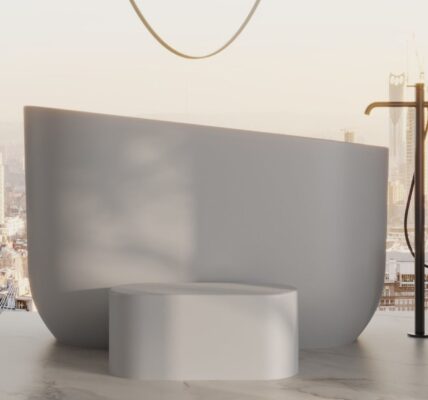 A minimalist, high-angle interior shot of a modern bathroom featuring a matte white stone Japanese soaking tub as the centrepiece. The tub has a sleek, asymmetrical rim that rises higher on one side, positioned in front of a floor-to-ceiling window overlooking a hazy city skyline at sunset.