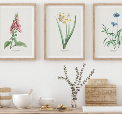 A trio of framed botanical art with Foxglove, Daffodils, and Cornflower prints hangs above a well-appointed light wood kitchen counter featuring assorted bowls, kitchen tools and a vase of eucalyptus.