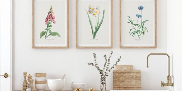 A trio of framed botanical art with Foxglove, Daffodils, and Cornflower prints hangs above a well-appointed light wood kitchen counter featuring assorted bowls, kitchen tools and a vase of eucalyptus.