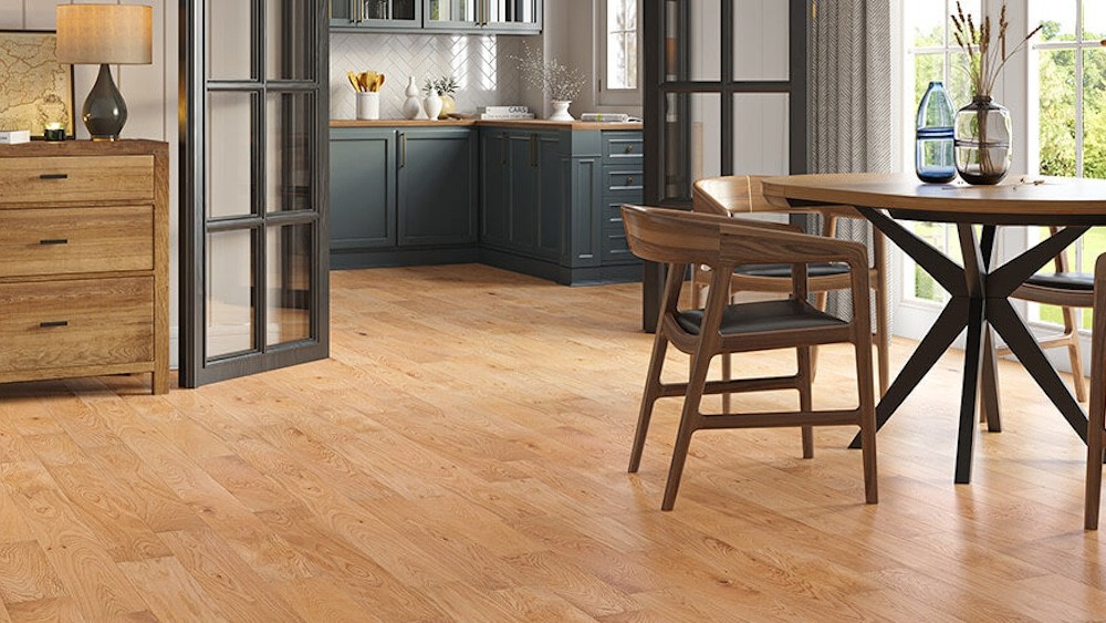A modern open-plan kitchen and dining area featuring warm Lusso Carrara Orchard engineered oak flooring, dark teal cabinetry, and mid-century modern wooden furniture.