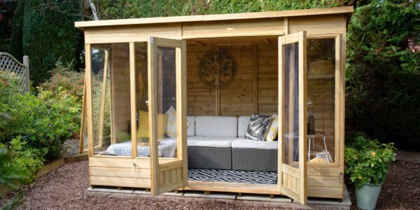 A wide-angle, eye-level shot shows a modern, light-wood Beckwood summerhouse nestled in a lush garden setting. The structure features double glass doors and large floor-to-ceiling windows, all of which are swung open to reveal an inviting interior.