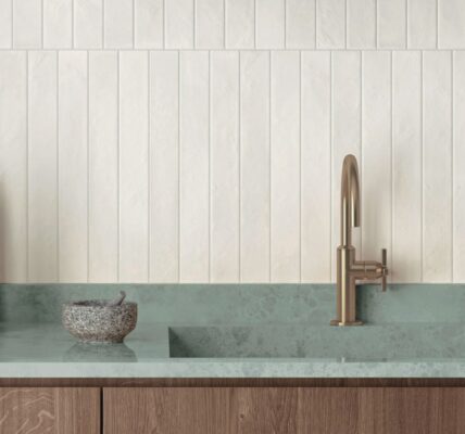 An eye-level, horizontal shot of a modern, minimalist kitchen features a vertical stack-bond backsplash made of textured, off-white rectangular tiles.