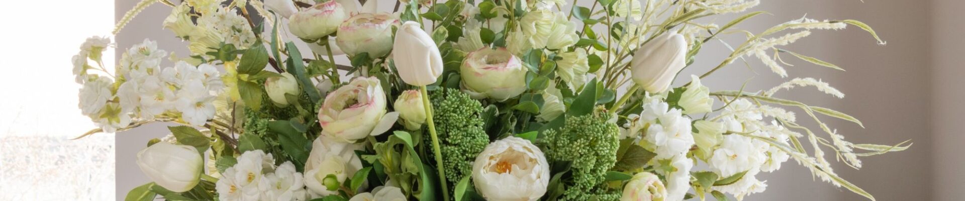 A lush, large floral arrangement in a white ceramic vase featuring a mix of white and cream-coloured flowers