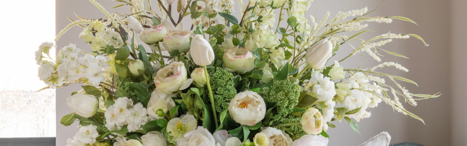 A lush, large floral arrangement in a white ceramic vase featuring a mix of white and cream-coloured flowers