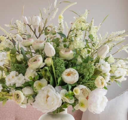A lush, large floral arrangement in a white ceramic vase featuring a mix of white and cream-coloured flowers