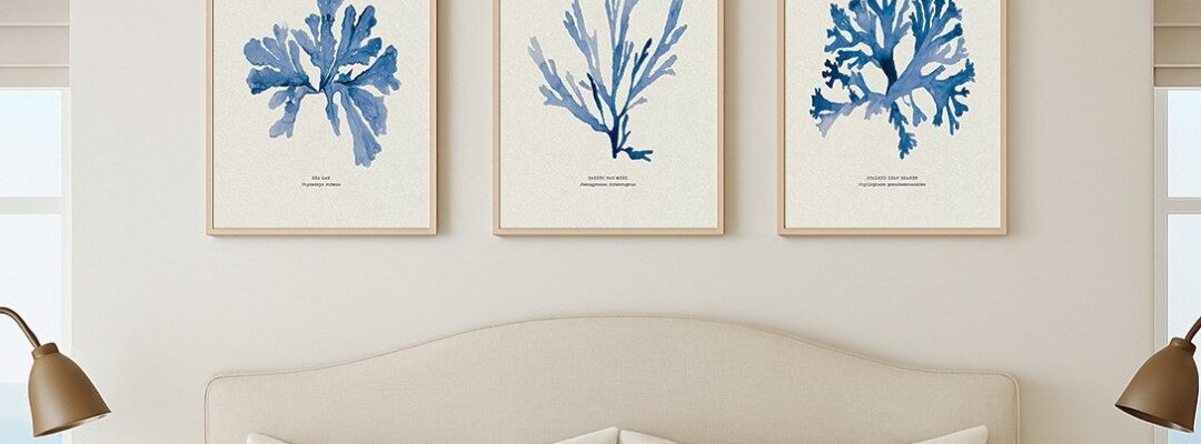 A wide landscape shot of a coastal-themed interior featuring a set of three botanical seaweed art prints hanging on an off-white wall. Below the artwork is a vibrant olive-green wainscoted wall, and in the foreground, a vintage-style brass bathtub faucet and shower head are partially visible, suggesting a sophisticated, spa-like bathroom setting. Soft, natural sunlight casts gentle shadows across the scene from the right.