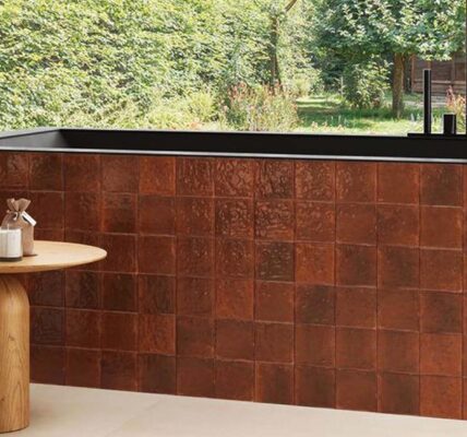 A wide, high-angle shot of a modern, spa-like bathroom featuring a rectangular bathtub clad in glossy, amber-coloured terracotta tiles