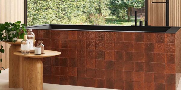 A wide, high-angle shot of a modern, spa-like bathroom featuring a rectangular bathtub clad in glossy, amber-coloured terracotta tiles
