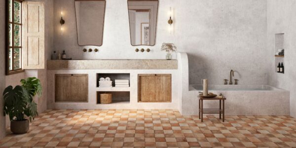 An interior photograph of a spacious, rustic-style bathroom featuring earthy tones and Mediterranean influences. The foreground is dominated by a chequerboard pattern of terracotta floor tiles in varying shades of burnt orange, tan, and cream.