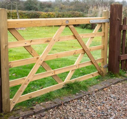 A 7ft light-coloured wooden five-bar gate installed between brick pillars, opening up to a green lawn in a countryside garden setting.