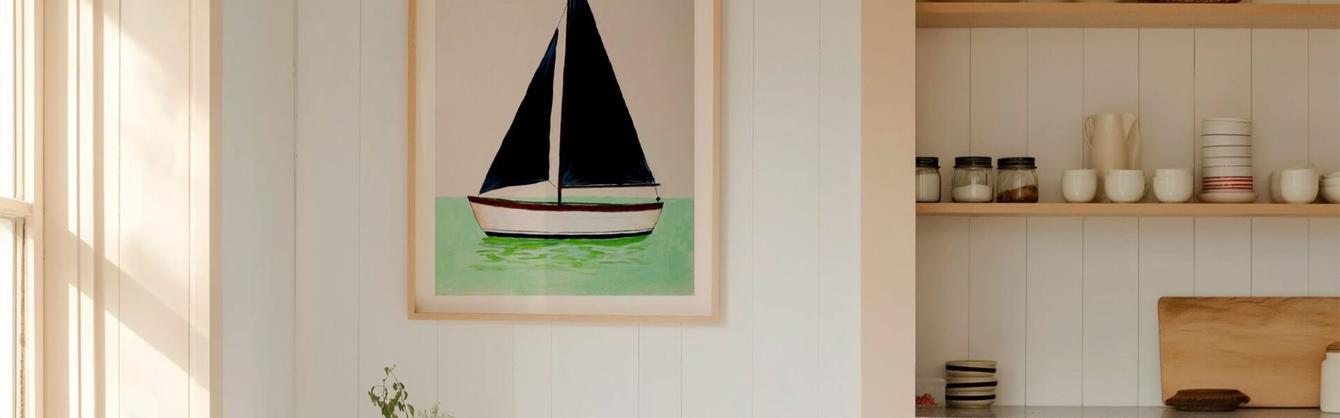 A framed art print of a minimalist sailboat with dark navy blue sails, floating on mint green water against a light beige background. The vertical print is housed in a light wood frame and hangs on a white, vertical-shiplap wall.
